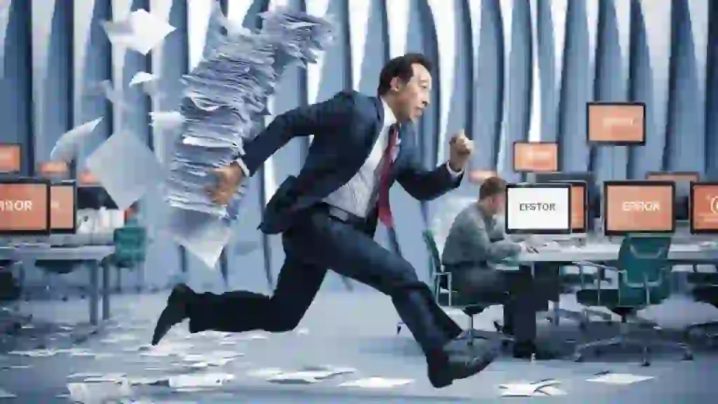 A business person running frantically holding a stack of falling papers. This symbolizes the loss of productivity and chaos that computer failures can cause